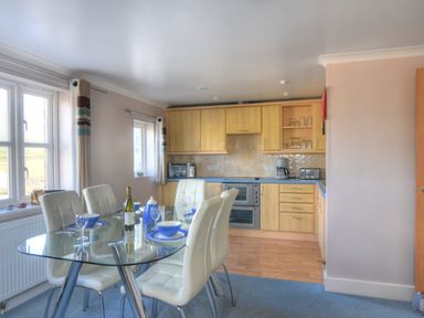 A kitchen with wooden cabinets glass dining table white chairs and blue dining set at 9 Maritime House in West Bay
