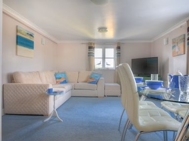 A living room with a beige sectional sofa and a round glass dining table with white chairs at 9 Maritime House in West Bay