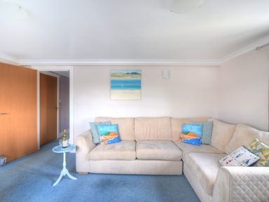A living room with beige sofa blue carpet small round blue table and a painting on the wall at 9 Maritime House in West Bay