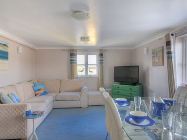 A living room with a beige corner sofa and a glass dining table set with blue and white dishes at 9 Maritime House in West Bay