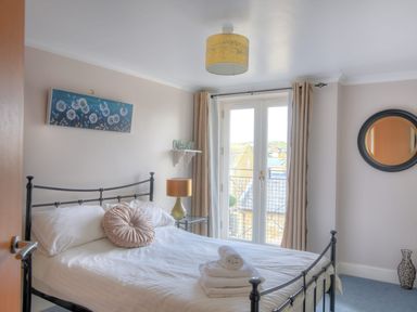 A bedroom with a metal bed frame white bedding round pillow bedside table lamp wall art a mirror and French doors at 9 Maritime House in West Bay