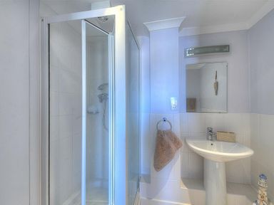 A bathroom with a corner shower enclosure a white pedestal sink a mirror and a towel hanging on a ring at 9 Maritime House in West Bay