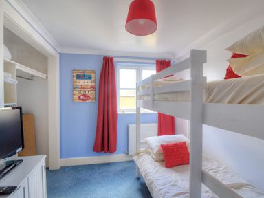 A bedroom with white bunk beds red curtains and a blue carpet at 9 Maritime House in West Bay