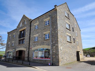 A stone building with multiple windows and a shopfront on a street at 9 Maritime House in West Bay