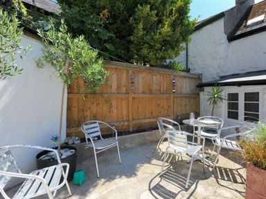 An outdoor patio with metal chairs and a table near a wooden fence and white building at Monmouth Cottage in Lyme Regis