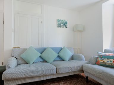 A living room with a striped sofa with cushions a floor lamp and a small painting on the wall at Monmouth Cottage in Lyme Regis