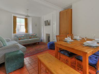A living room with sofas a wooden dining table with chairs and blue cushions at Monmouth Cottage in Lyme Regis