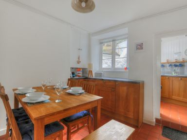 A dining area with a wooden table set with bowls and glasses next to a kitchen with wooden cabinets at Monmouth Cottage in Lyme Regis