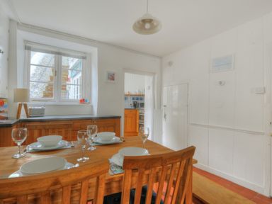 A dining room with a wooden table set with dishes and glasses near a window and a doorway to the kitchen at Monmouth Cottage in Lyme Regis