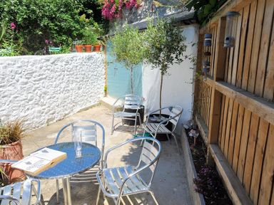 An outdoor patio with metal chairs and a table next to a white textured wall and wooden fence at Monmouth Cottage in Lyme Regis