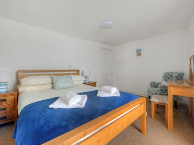A bedroom with a wooden bed covered with towels bedside tables lamps and a wooden dressing table with an armchair at Monmouth Cottage in Lyme Regis