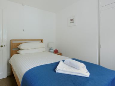 A bedroom with a single bed with white sheets and a blue blanket folded towels on the bed and a bedside table with a lamp and clock at Monmouth Cottage in Lyme Regis
