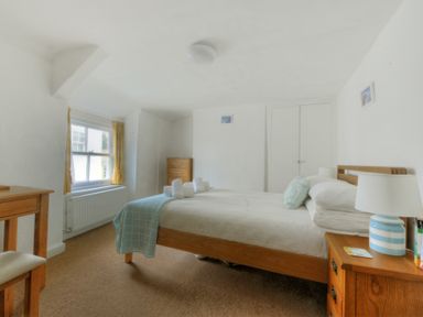 A bedroom with a bed side table a wooden chair bed and chest of drawers at Monmouth Cottage in Lyme Regis