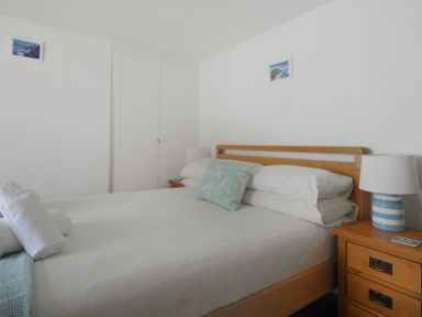 A bedroom with a bed white bedding and wooden headboard two bedside tables lamps and two small pictures on the wall at Monmouth Cottage in Lyme Regis