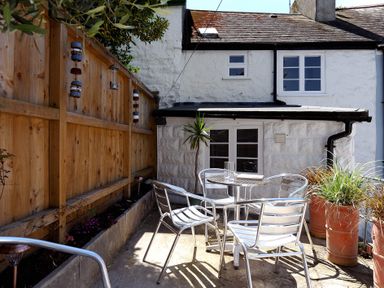 An outdoor patio area with a round metal table and four metal chairs beside a white stone building at Monmouth Cottage in Lyme Regis