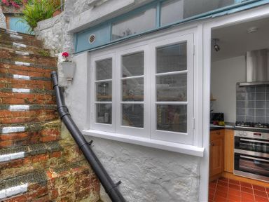 An outdoor brick staircase next to a white wall with windows showing a kitchen interior at Monmouth Cottage in Lyme Regis