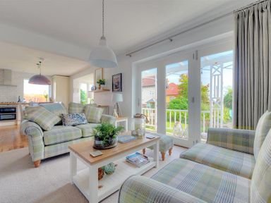A living room with plaid sofas a wooden coffee table and large glass doors looking out on a garden at Highpoint Lodge in Lyme Regis