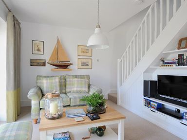 A living room with a plaid sofa a wooden coffee table decorative sailboat wall art and a television under stairs at Highpoint Lodge Lyme Regis