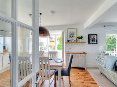 A dining area with a wooden table and chairs next to a living room with a couch and framed pictures at Highpoint Lodge in Lyme Regis