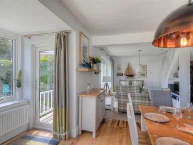 A dining area with a wooden table set with plates and glasses next to a living area with plaid sofas and wall decorations at Highpoint Lodge in Lyme Regis