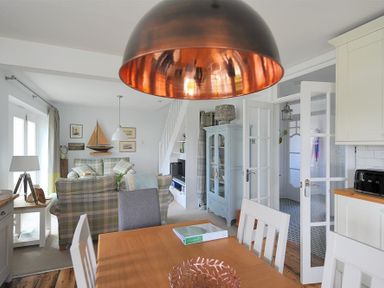 A dining table with chairs under a copper light fixture in a living room with a plaid sofa and decorative sailboat at Highpoint Lodge in Lyme Regis