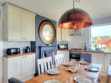 A kitchen with white cabinets a wooden dining table set with plates and glasses and a large round pendant light at Highpoint Lodge in Lyme Regis