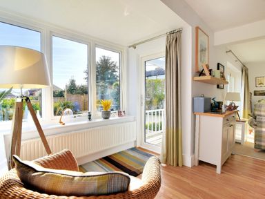 A sunroom with large windows wicker chair floor lamp and a door leading outside at Highpoint Lodge in Lyme Regis