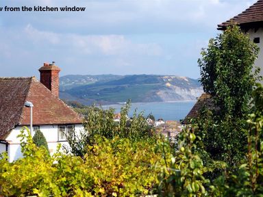 A view of rooftops trees and a coastline with hills in the distance at Highpoint Lodge in Lyme Regis
