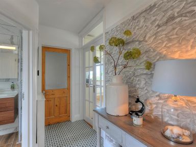 A hallway with a wooden door white walls patterned floor and a wooden table with a lamp plant and decorative items at Highpoint Lodge in Lyme Regis