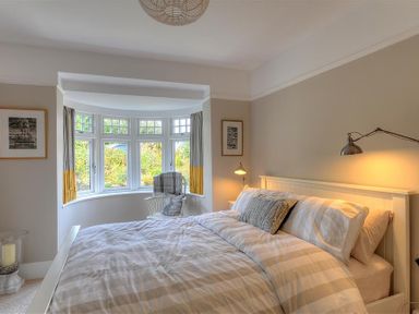 A bedroom with a bed lamps a chair by a bay window and framed pictures on walls at Highpoint Lodge in Lyme Regis