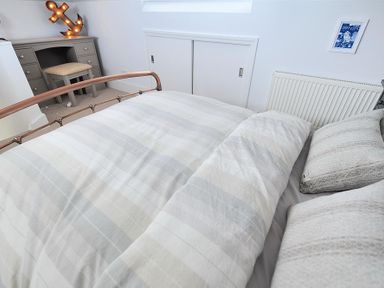 A bedroom with a bed featuring plaid bedding a gray desk with a small stool and a lighted anchor decoration at Highpoint Lodge in Lyme Regis