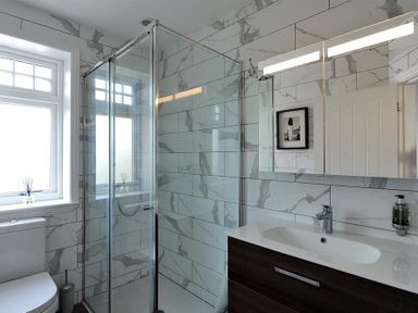 A bathroom with a glass shower enclosure, a toilet next to a window, a dark wood vanity with a white sink, and a mirrored cabinet on the wall at Highpoint Lodge in Lyme Regis