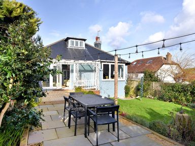 A backyard patio with a dining table and chairs next to a blue house with a sloped roof at Highpoint Lodge in Lyme Regis