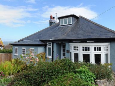 A single-story house with a slate roof surrounded by a garden with various plants and flowers at Highpoint Lodge in Lyme Regis