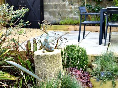 A garden with a stone pedestal holding a metal frog sculpture and patio furniture at Highpoint Lodge in Lyme Regis