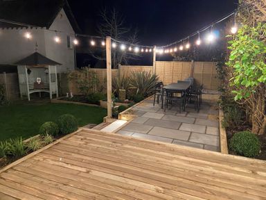 A backyard with a wooden deck a stone patio with a dining table and string lights at Highpoint Lodge in Lyme Regis