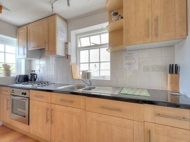 A kitchen with wooden cabinets a stove a sink knives and cooking utensils at Bay View in Lyme Regis