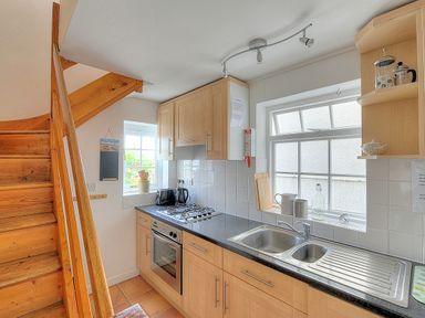 A kitchen with wooden cabinets a gas stove oven a double sink and staircase at Bay View in Lyme Regis