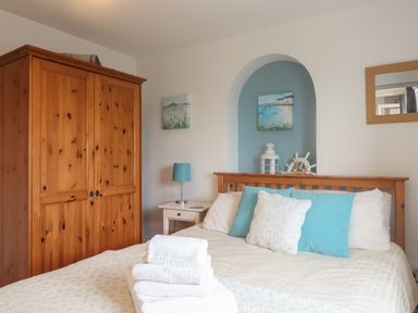 A bedroom with a wooden wardrobe a bed with blue and white pillows a white bedside table with a blue lamp and folded white towels on the bed at Bay View in Lyme Regis
