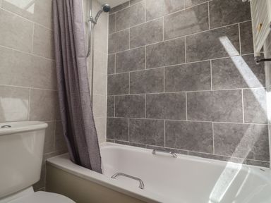 A bathroom with a bathtub shower combination a gray shower curtain and a toilet at Bay View Lyme Regis