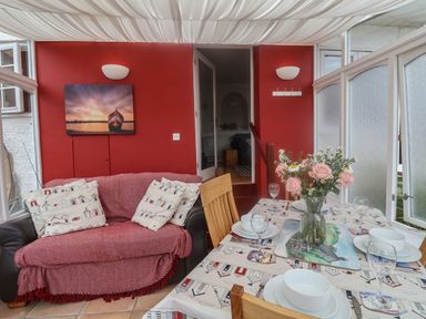 A dining area with a table set for four and a sofa with cushions against a red wall at Bay View in Lyme Regis