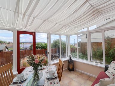 A dining area with a table set and flowers with windows and a red door at Bay View in Lyme Regis