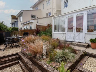 A garden with plants and a small statue next to a house with glass doors and patio chairs at Bay View in Lyme Regis