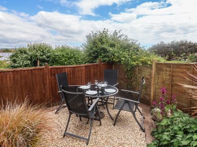 A small outdoor patio area with a round glass table set with plates and glasses and four black chairs surrounded by wooden fencing and plants at Bay View in Lyme Regis