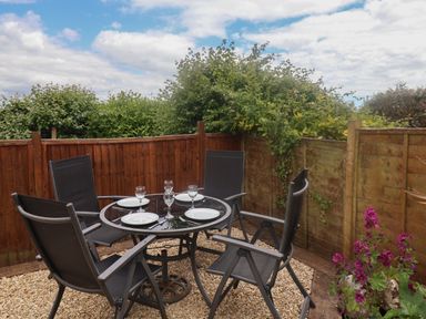 An outdoor patio area with a round glass table set with plates and glasses and four black chairs at Bay View in Lyme Regis