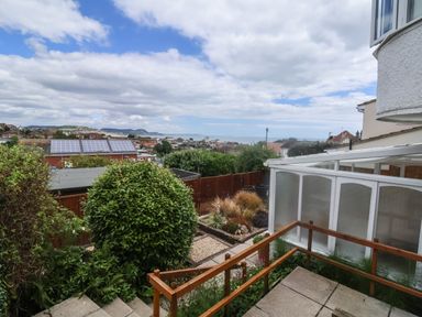 A garden with bushes and a wooden fence overlooking rooftops with solar panels and hills in the distance at Bay View in Lyme Regis