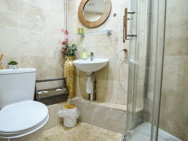 A bathroom with a toilet sink glass shower a round mirror and a tall vase with flowers at Cleve Cottage in Lyme Regis