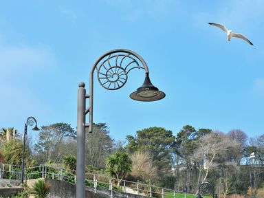 A street lamp with a spiral design with trees and a bird flying in the sky at Cleve Cottage in Lyme Regis