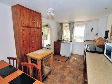 A kitchen with wooden cabinets a small island microwave dishwasher and a door with curtains at Willows in Charmouth
