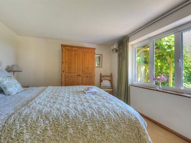 A bedroom with a bed a wooden wardrobe a chair with towels and a window with green curtains at Willows in Charmouth